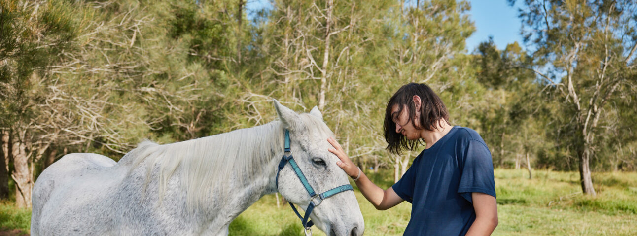 A girl is patting a white horse outdoors. Make a gift to Human Nature and support youth mental health.